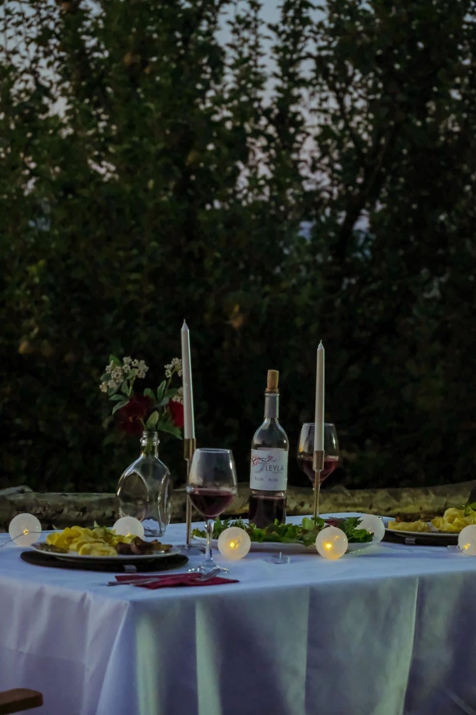 An outdoor table in a white cloth set with candles