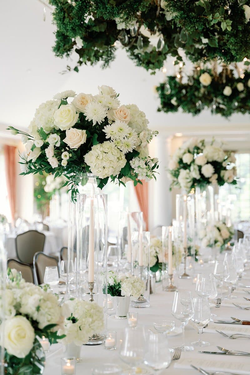 Tall white floral centrepieces on a long reception table (stock photo)